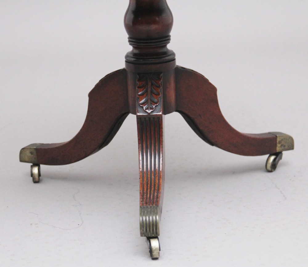 An early 19th-century Regency mahogany teapoy with a hinged tapered box mounted on a turned pedestal and reeded tripod legs with brass castors. View X