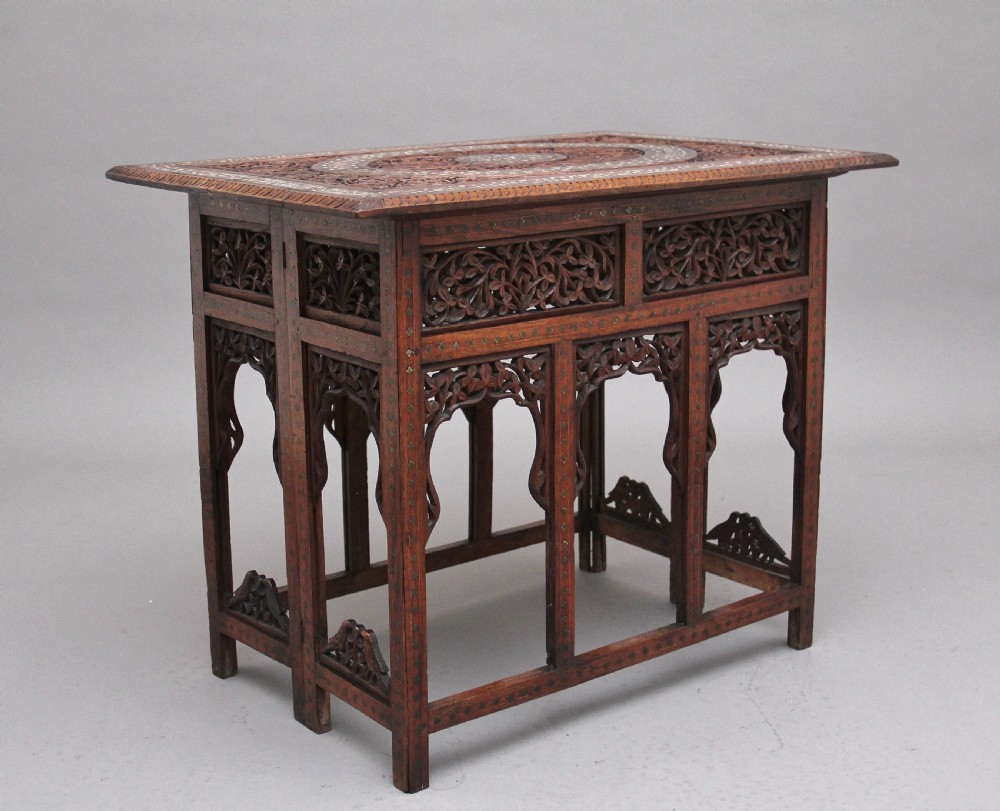 A 19th-century dark hardwood Indian occasional table featuring intricately carved floral fretwork panels, cusped arches, and a geometric bone-inlaid tabletop.