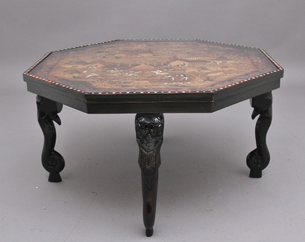 An octagonal wooden coffee table featuring detailed pictorial wood marquetry depicting an Indian village scene surrounded by a relief-carved floral border and ebonised outer rim. View II