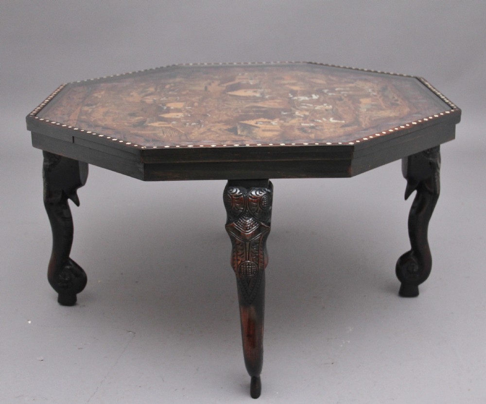 An octagonal wooden coffee table featuring detailed pictorial wood marquetry depicting an Indian village scene surrounded by a relief-carved floral border and ebonised outer rim. View IV