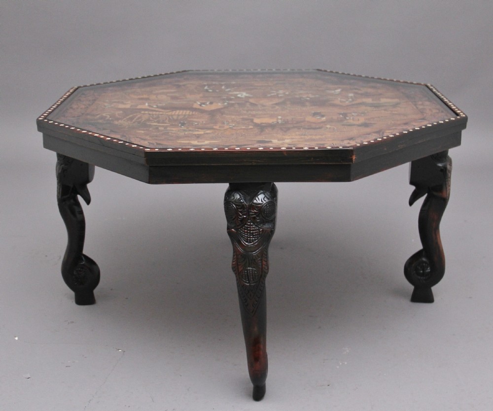 An octagonal wooden coffee table featuring detailed pictorial wood marquetry depicting an Indian village scene surrounded by a relief-carved floral border and ebonised outer rim. View V