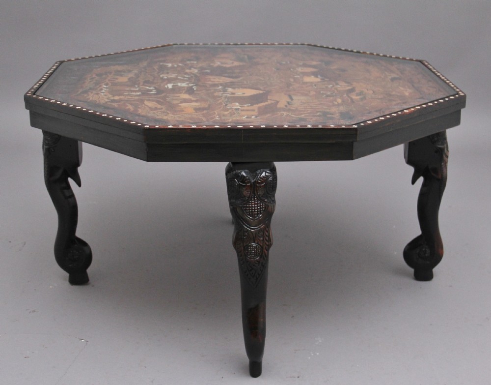 An octagonal wooden coffee table featuring detailed pictorial wood marquetry depicting an Indian village scene surrounded by a relief-carved floral border and ebonised outer rim. View VI