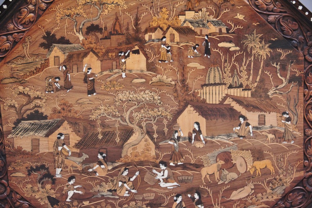 An octagonal wooden coffee table featuring detailed pictorial wood marquetry depicting an Indian village scene surrounded by a relief-carved floral border and ebonised outer rim. View VII
