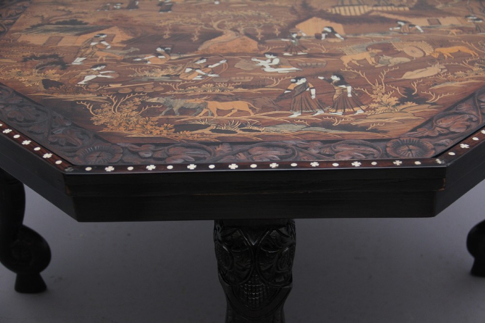 An octagonal wooden coffee table featuring detailed pictorial wood marquetry depicting an Indian village scene surrounded by a relief-carved floral border and ebonised outer rim. View IX