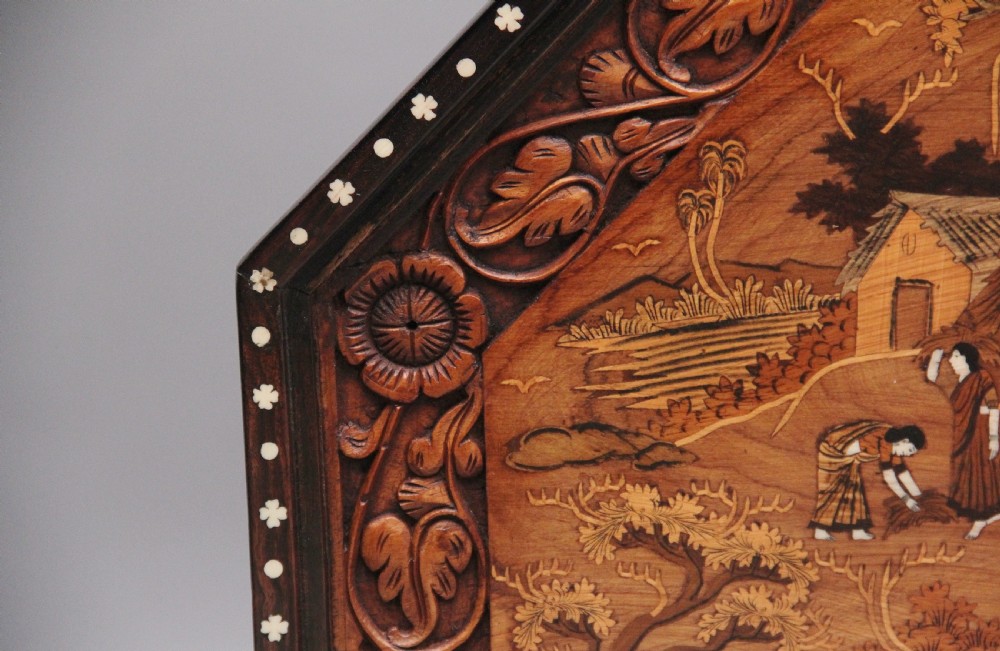 An octagonal wooden coffee table featuring detailed pictorial wood marquetry depicting an Indian village scene surrounded by a relief-carved floral border and ebonised outer rim. View XII
