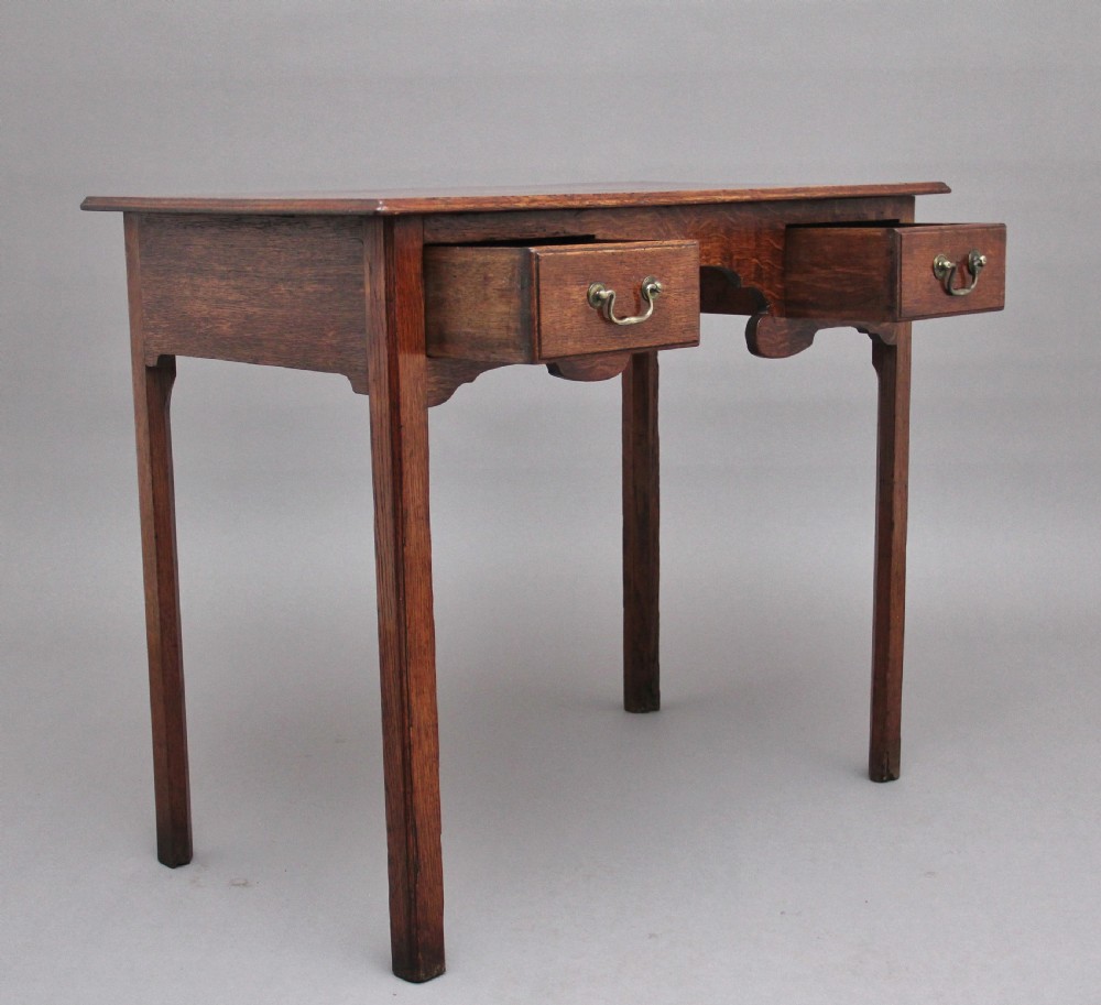 An early 19th-century oak lowboy side table featuring two drawers with brass handles, a shaped lower apron, and four straight legs. View V