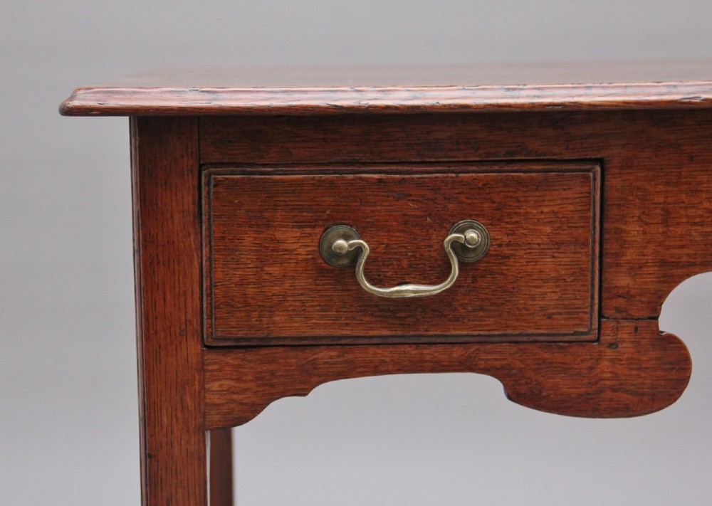 An early 19th-century oak lowboy side table featuring two drawers with brass handles, a shaped lower apron, and four straight legs. View VI