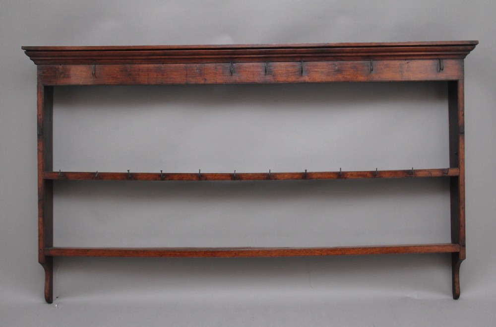 An 18th-century oak wall-mounted hanging rack featuring a moulded top cornice, open shelves, and embedded iron hooks.