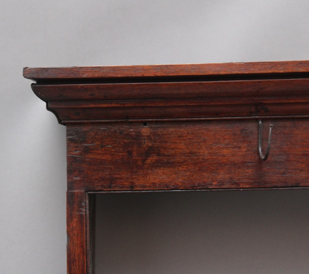 An 18th-century oak wall-mounted hanging rack featuring a moulded top cornice, open shelves, and embedded iron hooks. View II