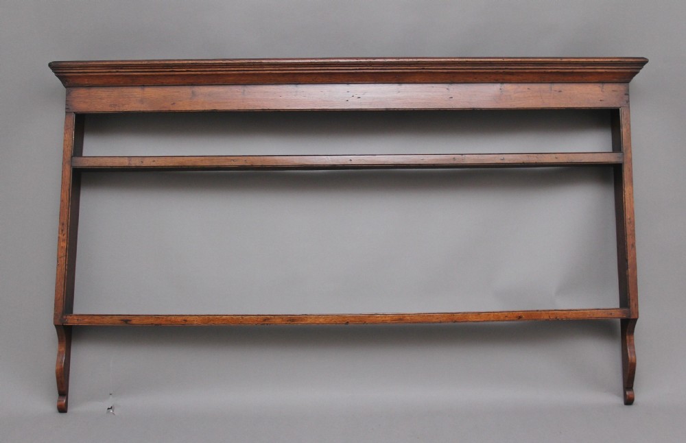 An 18th-century oak wall-mounted plate rack featuring a moulded top cornice, horizontal display shelves, and shaped side supports in a warm brown timber finish.