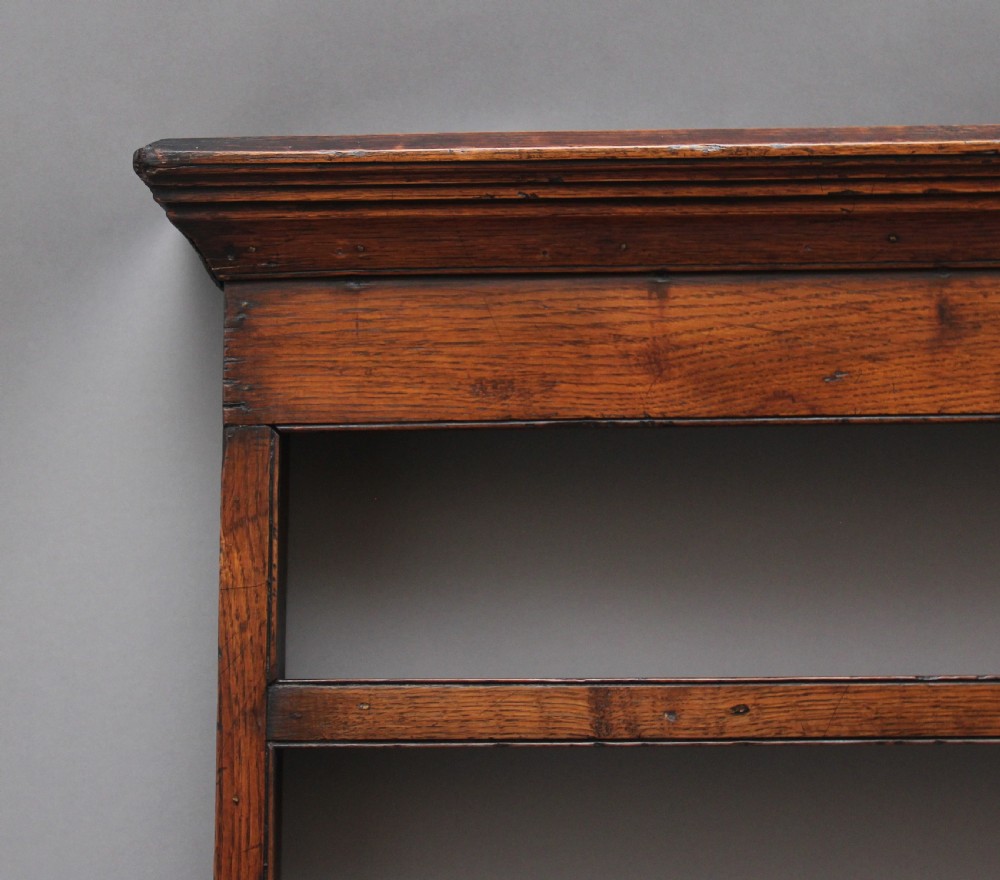 An 18th-century oak wall-mounted plate rack featuring a moulded top cornice, horizontal display shelves, and shaped side supports in a warm brown timber finish. View II