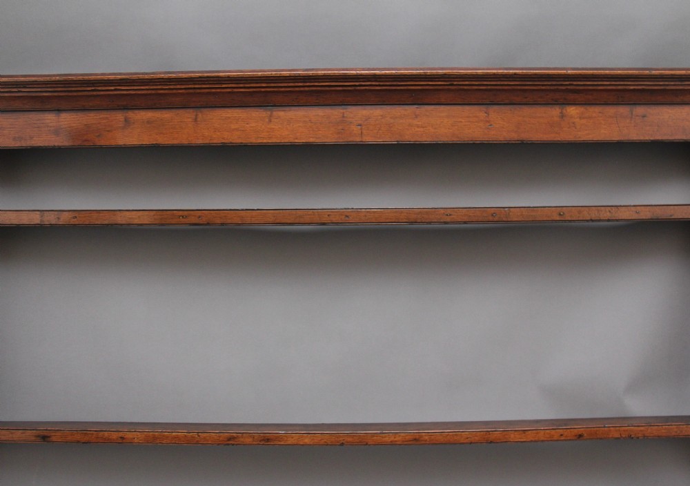 An 18th-century oak wall-mounted plate rack featuring a moulded top cornice, horizontal display shelves, and shaped side supports in a warm brown timber finish. View III