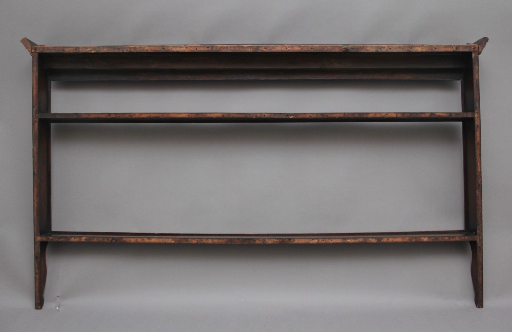 An 18th-century oak wall-mounted plate rack featuring a moulded top cornice, horizontal display shelves, and shaped side supports in a warm brown timber finish. View VI