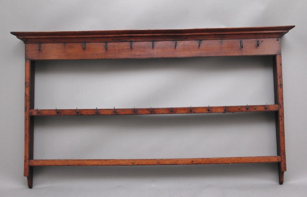 An 18th-century dark oak wall-mounted hanging rack featuring a moulded top cornice and two horizontal rails set with metal hooks.