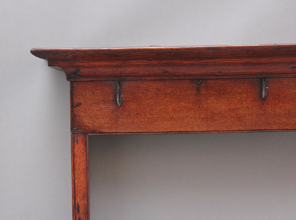 An 18th-century dark oak wall-mounted hanging rack featuring a moulded top cornice and two horizontal rails set with metal hooks. View II