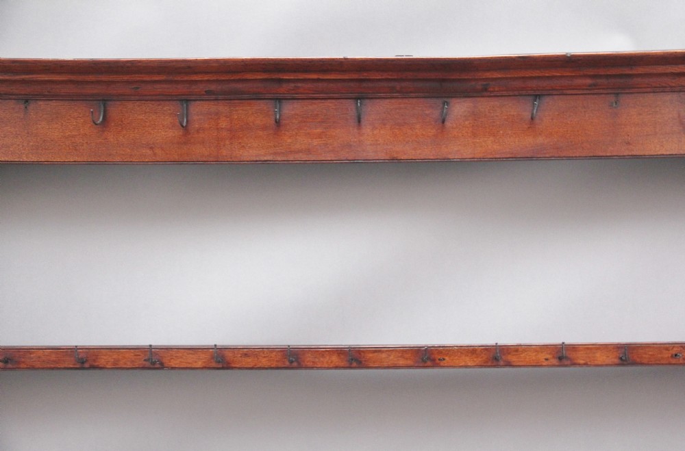 An 18th-century dark oak wall-mounted hanging rack featuring a moulded top cornice and two horizontal rails set with metal hooks. View III