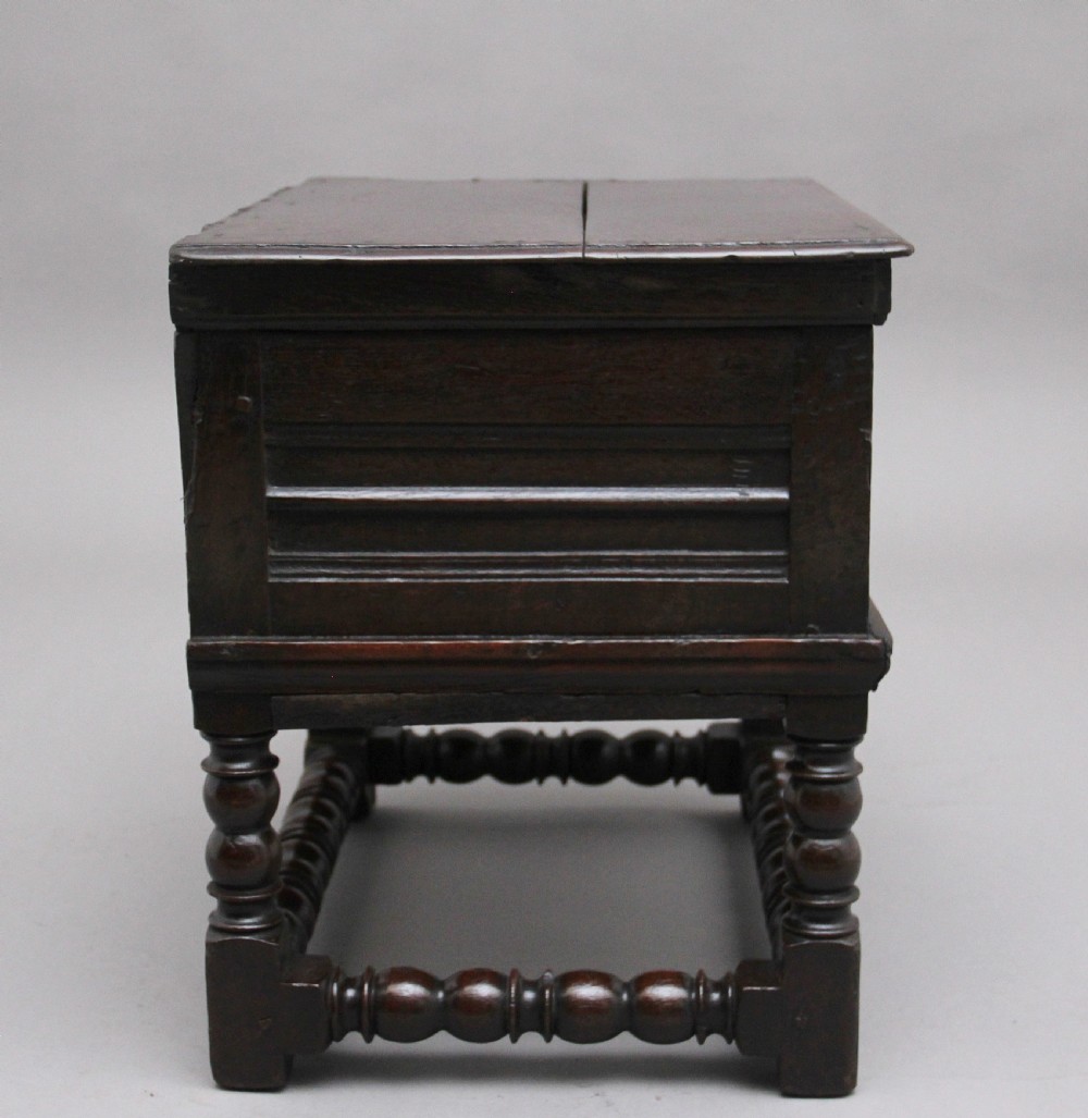 An early 18th-century dark oak box stool featuring a hinged lid, moulded side panels, and turned legs joined by stretchers. View III