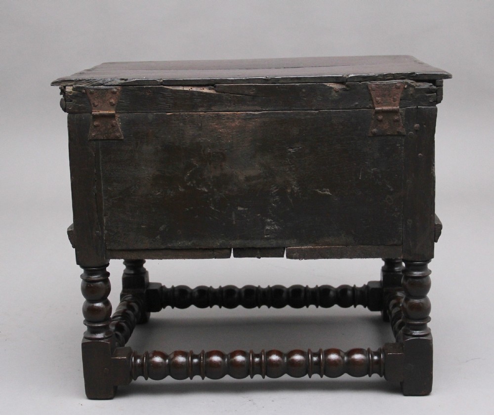 An early 18th-century dark oak box stool featuring a hinged lid, moulded side panels, and turned legs joined by stretchers. View IV