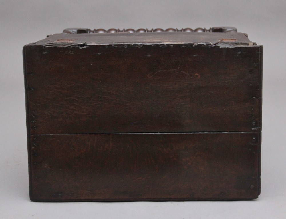 An early 18th-century dark oak box stool featuring a hinged lid, moulded side panels, and turned legs joined by stretchers. View VI