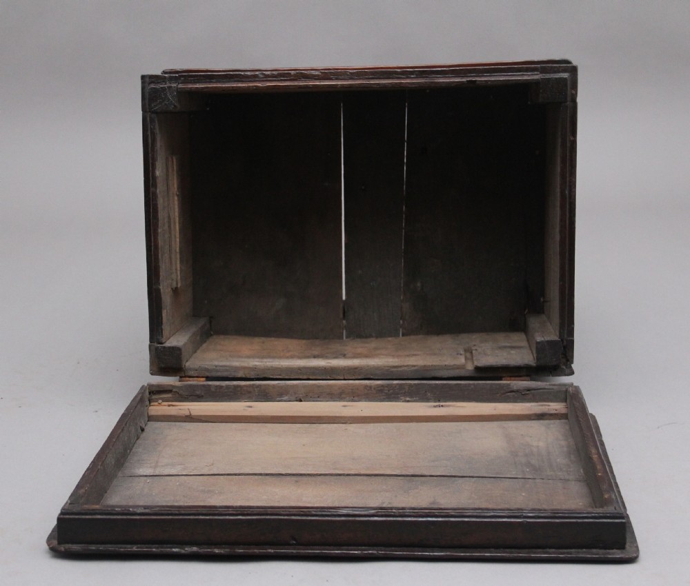 An early 18th-century dark oak box stool featuring a hinged lid, moulded side panels, and turned legs joined by stretchers. View VII