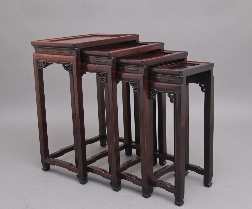 A graduating set of four dark hardwood Chinese nesting tables featuring carved corner spandrels and stepped stretchers.