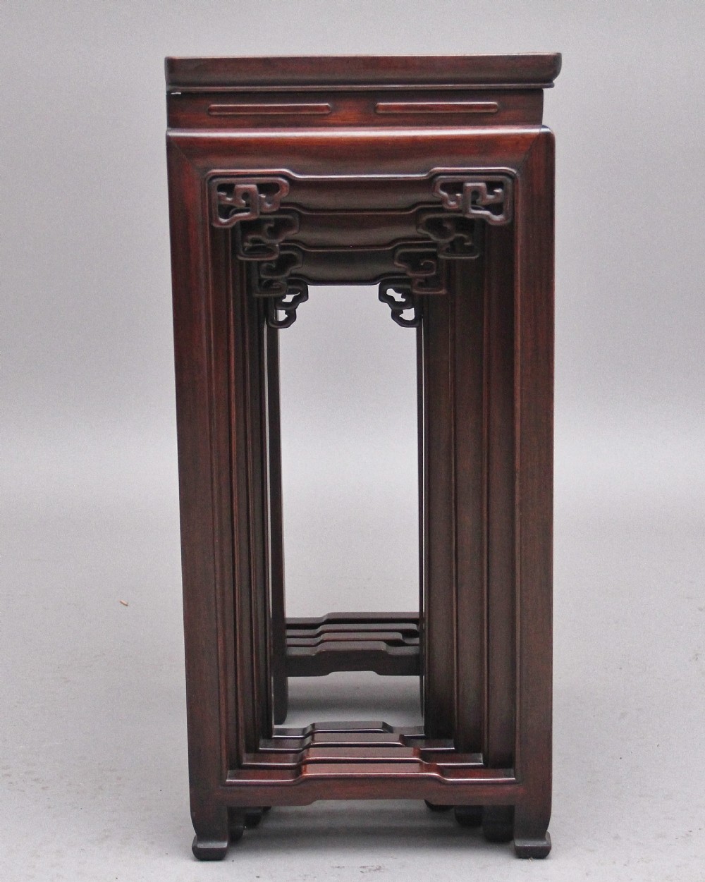 A graduating set of four dark hardwood Chinese nesting tables featuring carved corner spandrels and stepped stretchers. View V