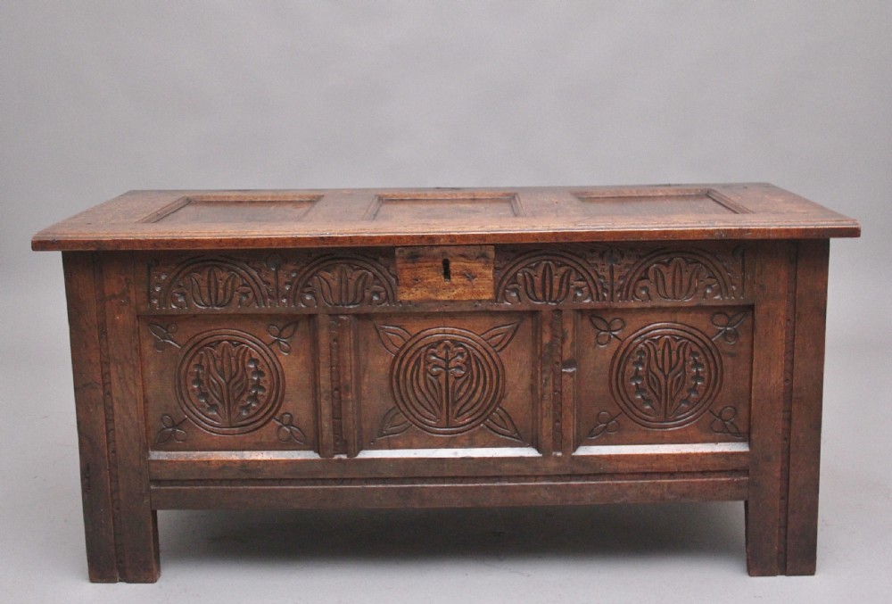 A 17th-century dark oak coffer featuring three carved geometric front panels and a paneled hinged top.