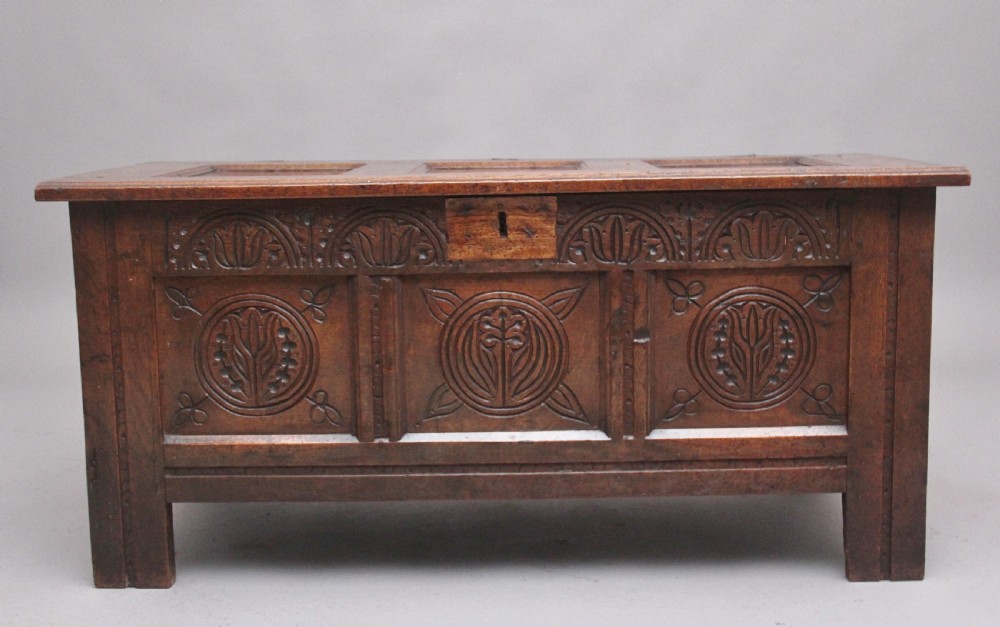 A 17th-century dark oak coffer featuring three carved geometric front panels and a paneled hinged top. View V