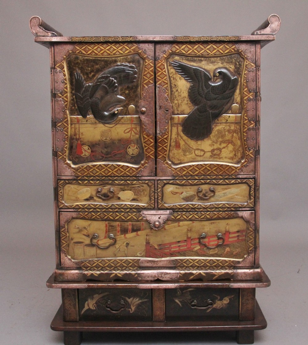 A 19th-century Japanese gilt lacquer tabletop cabinet featuring double doors with high-relief carved birds, several drawers, and decorative copper corner mounts.