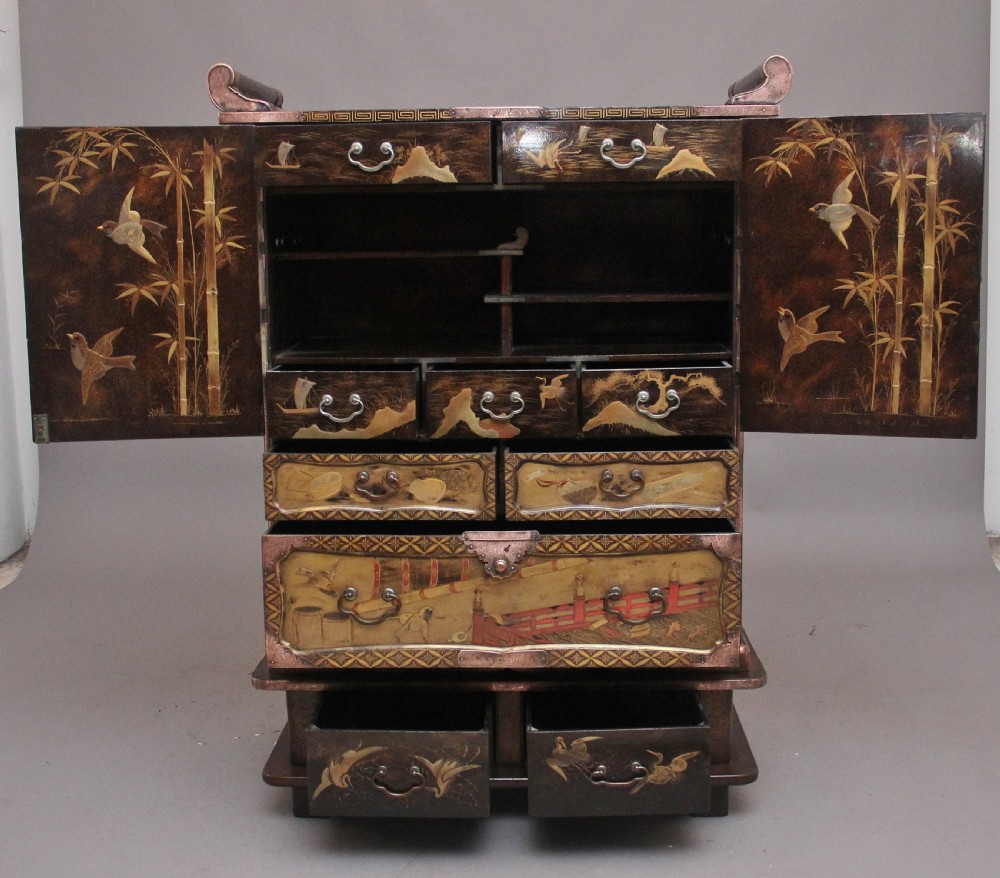 A 19th-century Japanese gilt lacquer tabletop cabinet featuring double doors with high-relief carved birds, several drawers, and decorative copper corner mounts. View IV