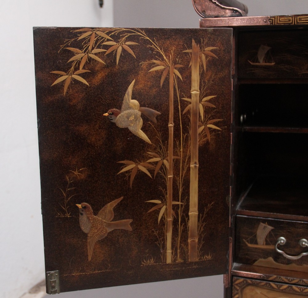 A 19th-century Japanese gilt lacquer tabletop cabinet featuring double doors with high-relief carved birds, several drawers, and decorative copper corner mounts. View XV
