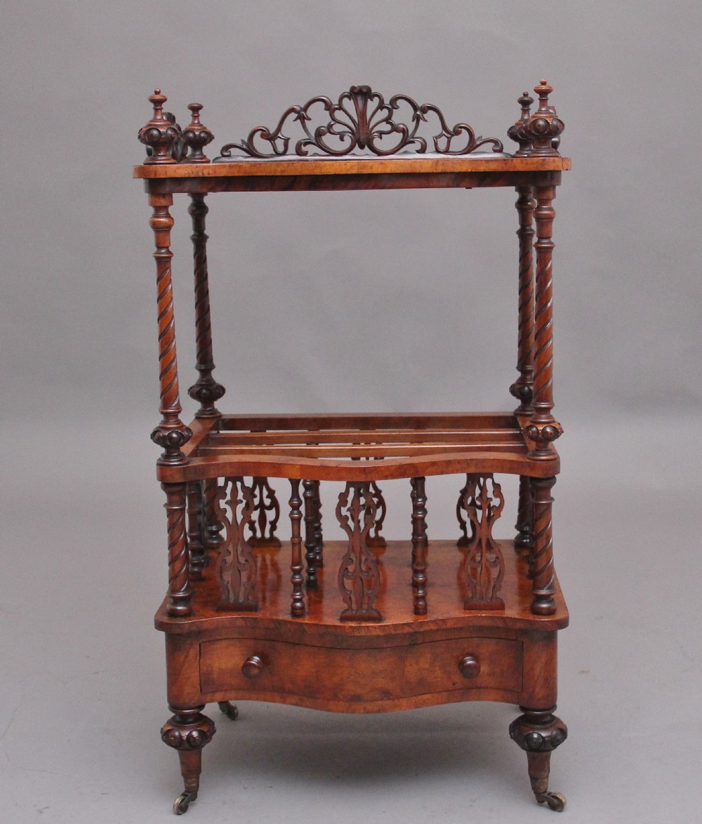 A 19th-century Victorian burr walnut music Canterbury featuring spiral twist support columns, pierced fretwork partitions, a serpentine lower drawer with turned wooden handles, and small brass castors.