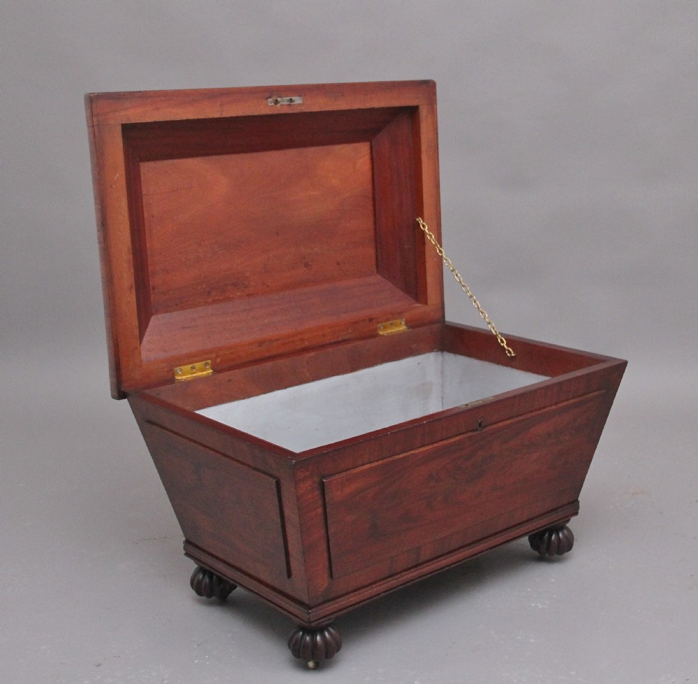 A 19th-century mahogany cellarette of sarcophagus form featuring a stepped lid, panelled sides, and carved gadrooned feet with castors. View II