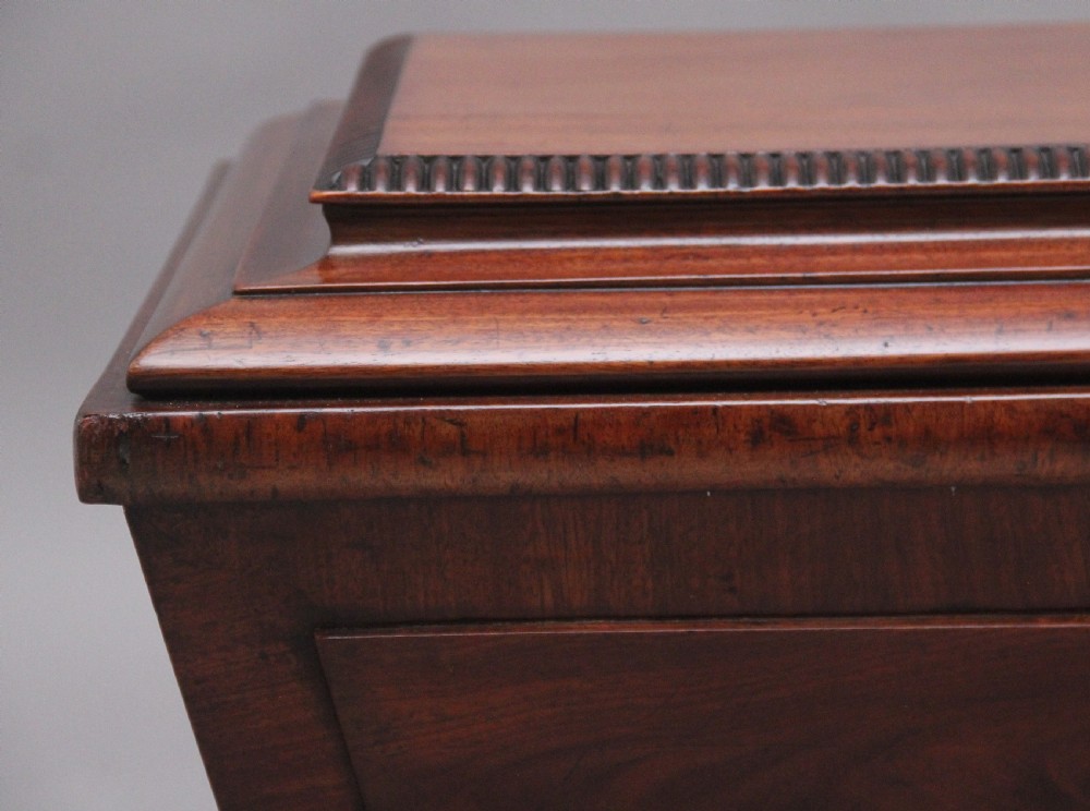 A 19th-century mahogany cellarette of sarcophagus form featuring a stepped lid, panelled sides, and carved gadrooned feet with castors. View X