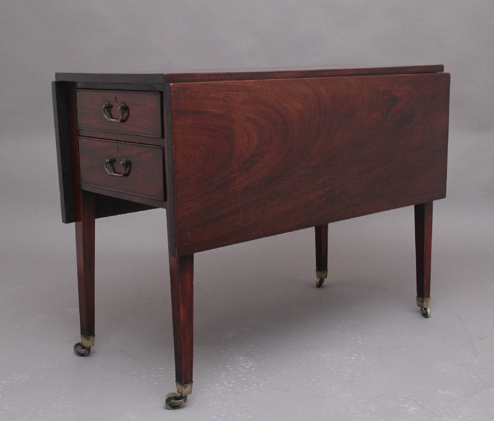 An 18th-century mahogany drop-leaf side table featuring two end drawers with brass bail handles and square tapered legs ending in brass castors.