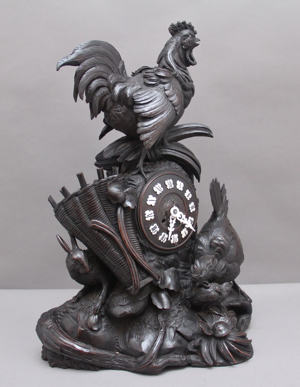 A 19th-century carved dark wood Black Forest mantel clock featuring a cockerel finial, foliage motifs, and a central circular clock face with Roman numerals. View II