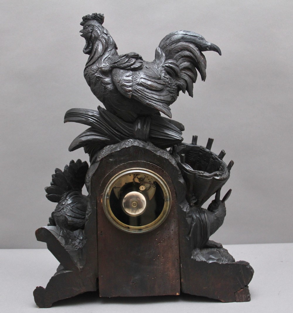 A 19th-century carved dark wood Black Forest mantel clock featuring a cockerel finial, foliage motifs, and a central circular clock face with Roman numerals. View V