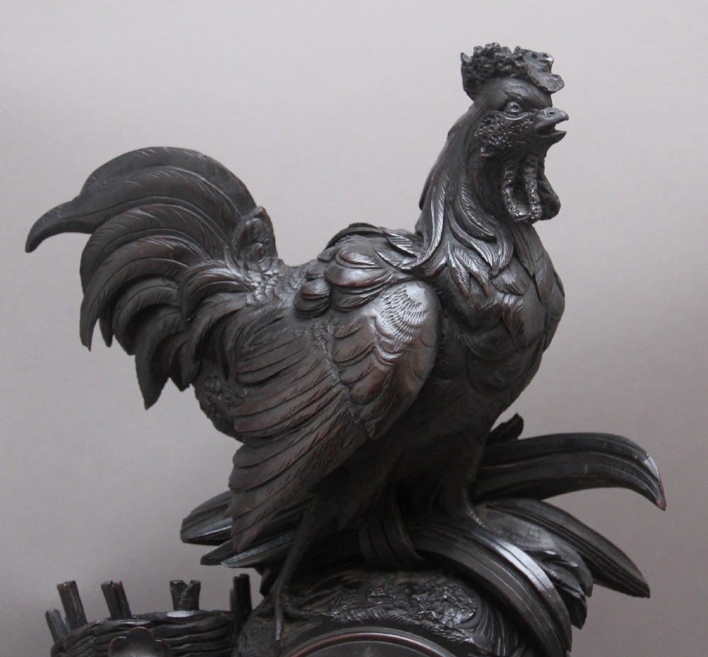 A 19th-century carved dark wood Black Forest mantel clock featuring a cockerel finial, foliage motifs, and a central circular clock face with Roman numerals. View VII