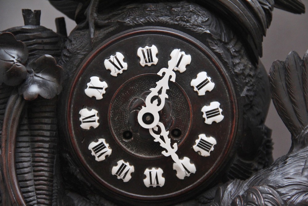 A 19th-century carved dark wood Black Forest mantel clock featuring a cockerel finial, foliage motifs, and a central circular clock face with Roman numerals. View IX