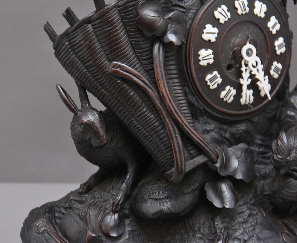 A 19th-century carved dark wood Black Forest mantel clock featuring a cockerel finial, foliage motifs, and a central circular clock face with Roman numerals. View X