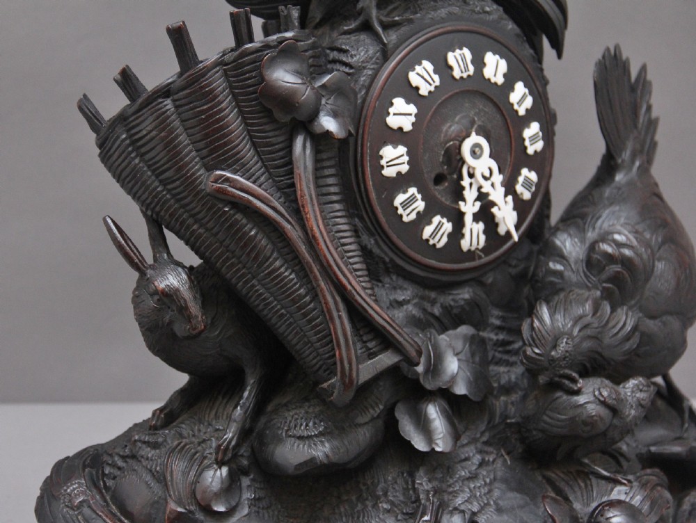 A 19th-century carved dark wood Black Forest mantel clock featuring a cockerel finial, foliage motifs, and a central circular clock face with Roman numerals. View XI