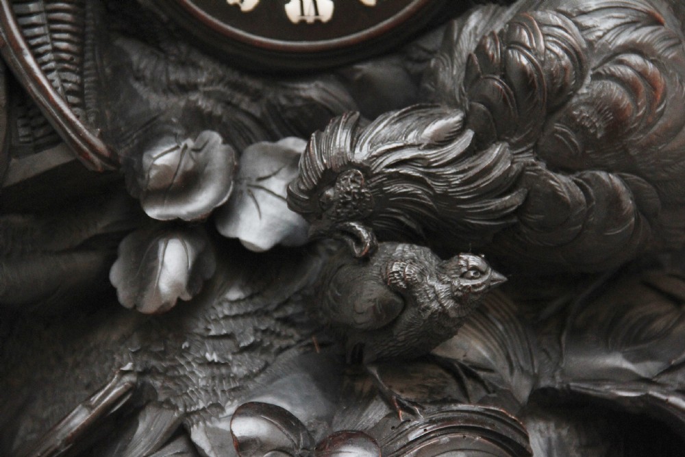 A 19th-century carved dark wood Black Forest mantel clock featuring a cockerel finial, foliage motifs, and a central circular clock face with Roman numerals. View XII