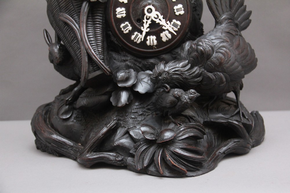 A 19th-century carved dark wood Black Forest mantel clock featuring a cockerel finial, foliage motifs, and a central circular clock face with Roman numerals. View XIV