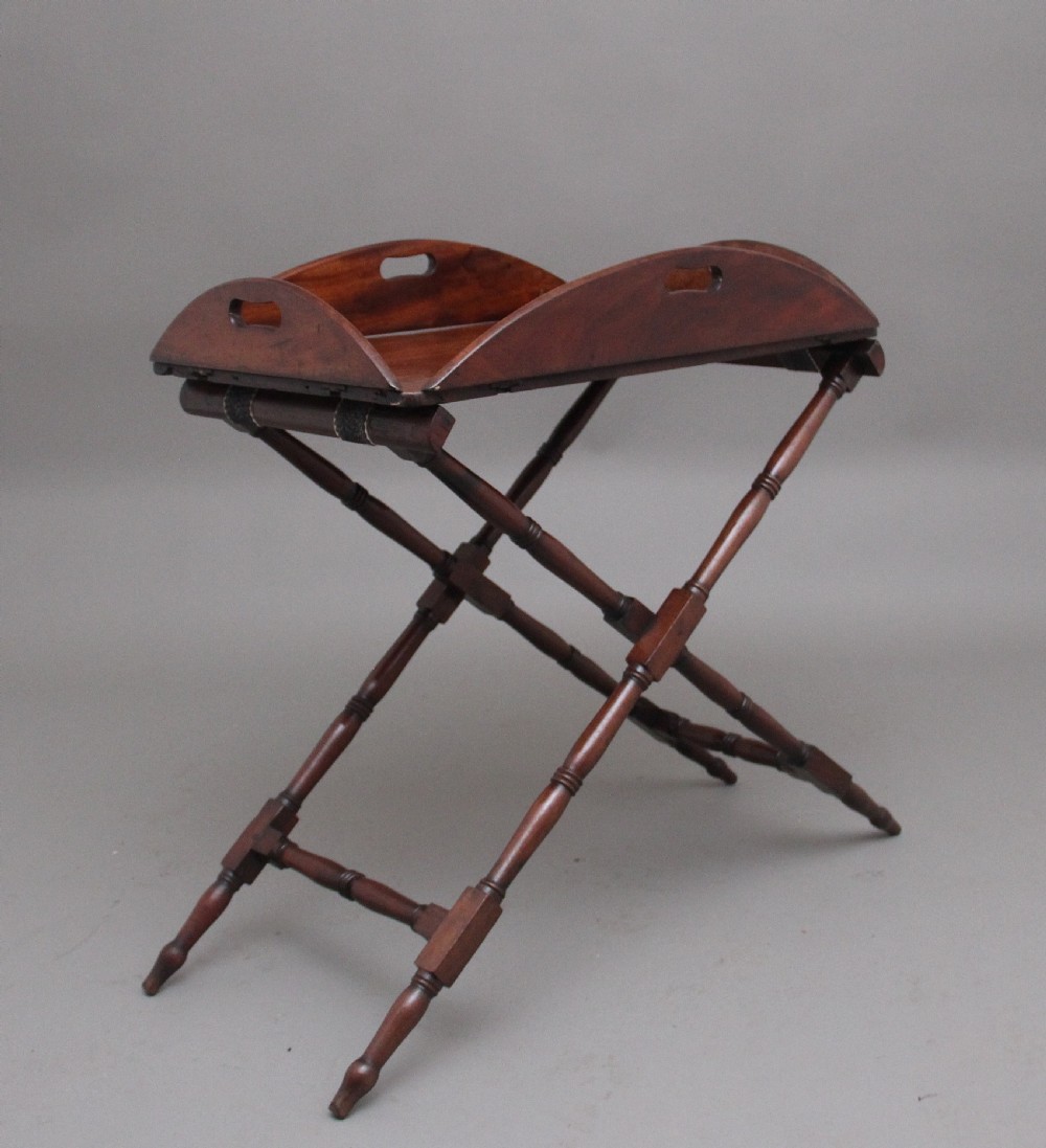 An early nineteenth-century dark mahogany butler tray with curved gallery sides and cut-out handles resting on a folding X-frame stand.