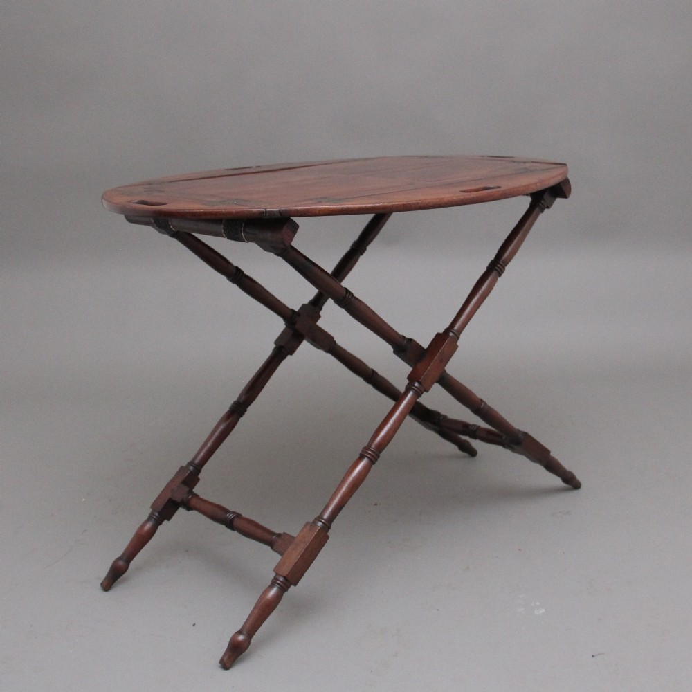 An early nineteenth-century dark mahogany butler tray with curved gallery sides and cut-out handles resting on a folding X-frame stand. View II