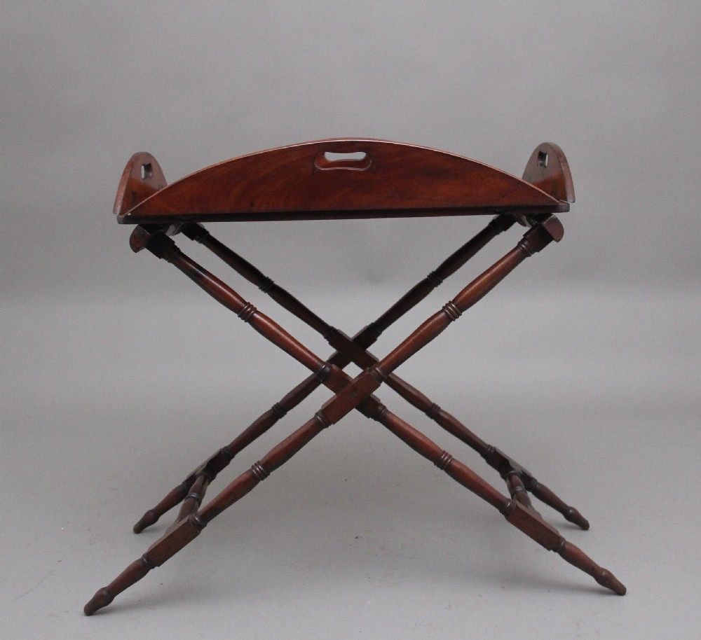 An early nineteenth-century dark mahogany butler tray with curved gallery sides and cut-out handles resting on a folding X-frame stand. View IV