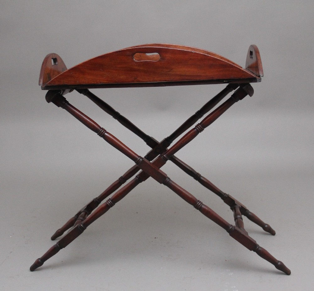 An early nineteenth-century dark mahogany butler tray with curved gallery sides and cut-out handles resting on a folding X-frame stand. View VI