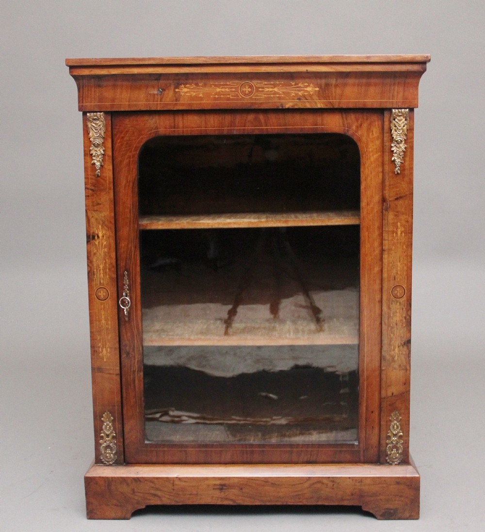 A 19th-century walnut pier cabinet featuring floral marquetry inlays, decorative brass mounts, and a single glazed door revealing fitted shelves.