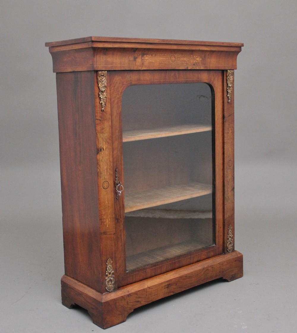A 19th-century walnut pier cabinet featuring floral marquetry inlays, decorative brass mounts, and a single glazed door revealing fitted shelves. View II