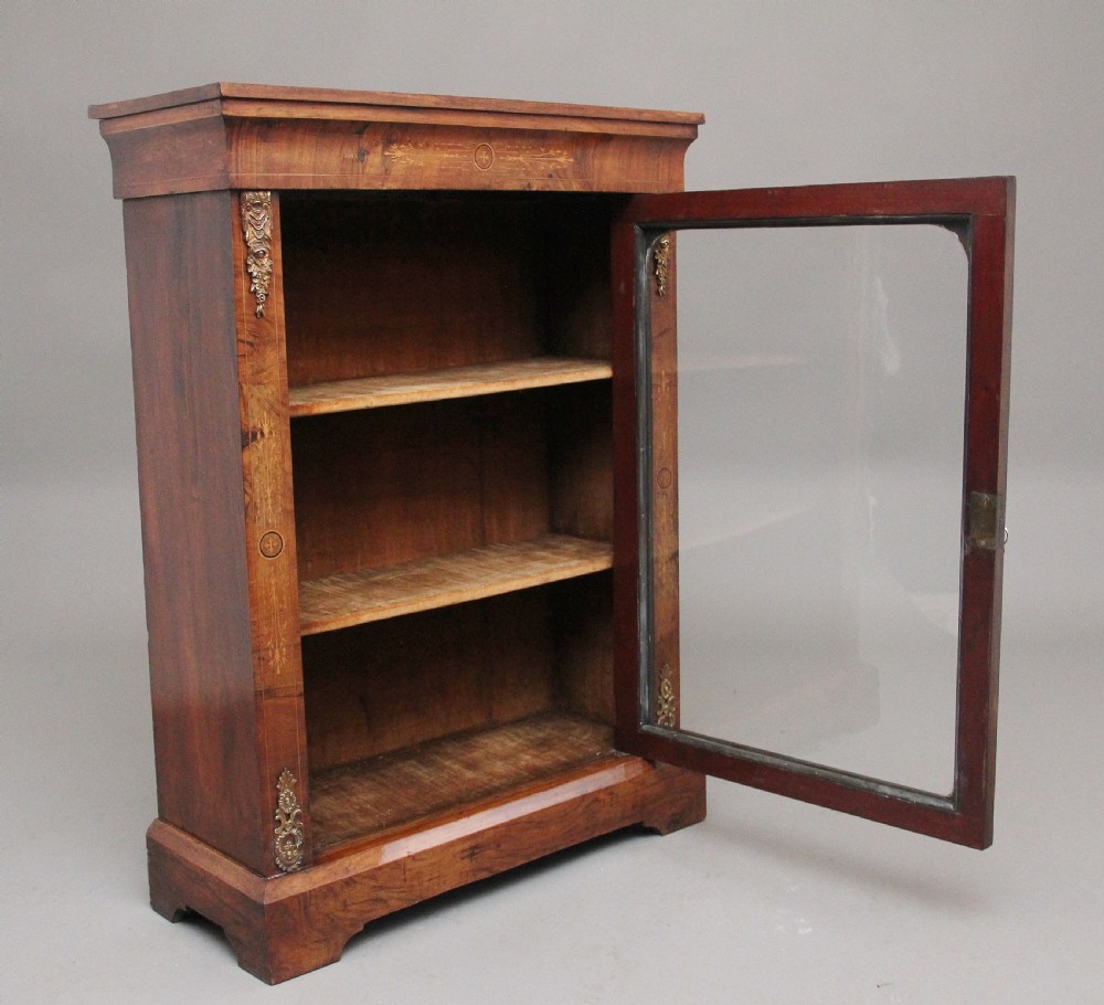 A 19th-century walnut pier cabinet featuring floral marquetry inlays, decorative brass mounts, and a single glazed door revealing fitted shelves. View III